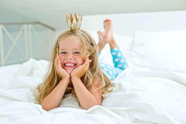 Niña sonriente con una corona tumbada en un colchón LoMonaco